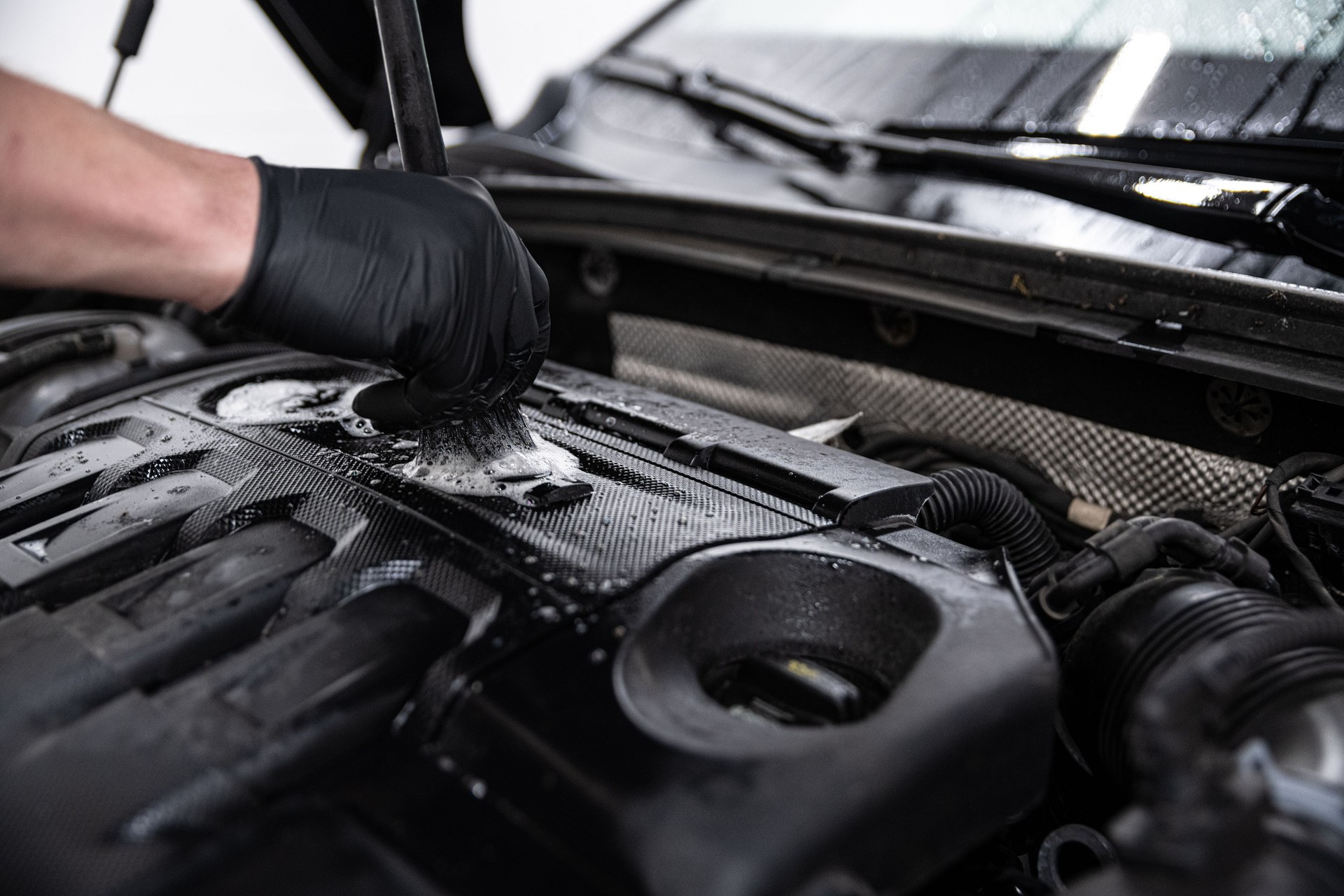Mechanic wearing black gloves cleaning a car engine in a detailing studio